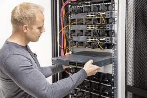 IT engineer or technician working with network cabling and installation communication switches in datacenter.